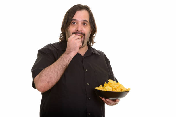 istock overweight bearded man holding while eating bowl of potato chips 668698140