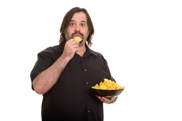 istock overweight bearded man eating bowl of potato chips 668698144