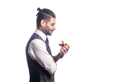 Handsome bearded businessman holding a glass of whiskey. side view. holding glass and smiling with closed eyes. studio shot, isolated on white background.