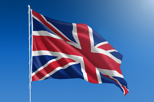 The National flag of United Kingdom of Great Britain blowing in the wind in front of a clear blue sky