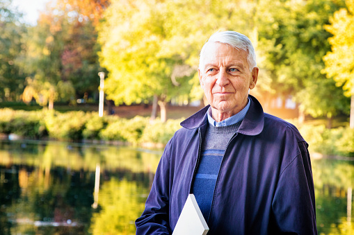 Senior male holding book in park on Autumn day