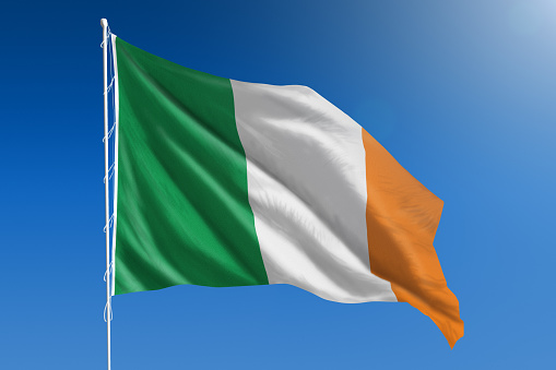 The National flag of Ireland blowing in the wind in front of a clear blue sky