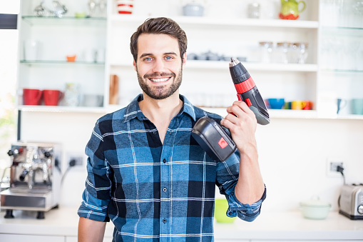 Portrait of happy man holding with drill machine in kitchen at home