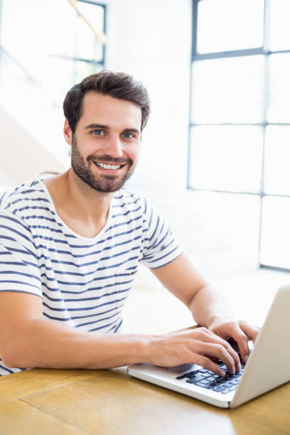 istock Portrait of happy man sitting on table and using laptop 668724416