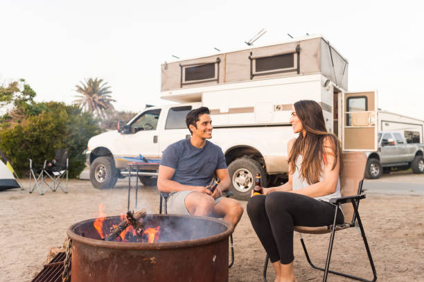 Couple Sitting By The Campfire At Sunset A Hispanic couple sitting by the campfire by the ocean. RV truck stock pictures, royalty-free photos & images
