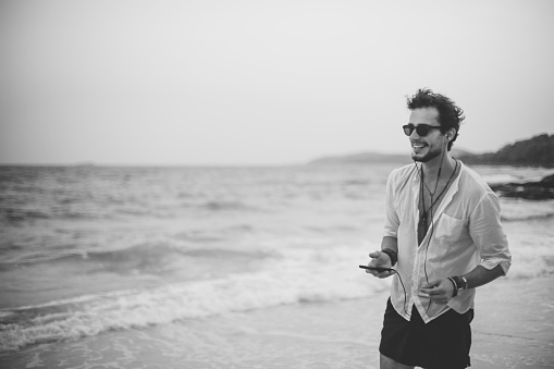 One man, man on the beach, listening music on smart phone, black and white.