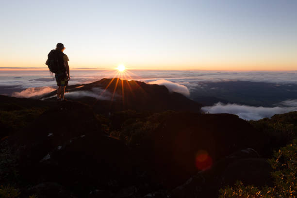 un alpinista guarda il sole sorgere sopra le nuvole da un alto punto panoramico - pinnacle foto e immagini stock