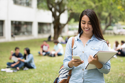 Portrait of a happy Latin American female student texting on her cell phone at the university