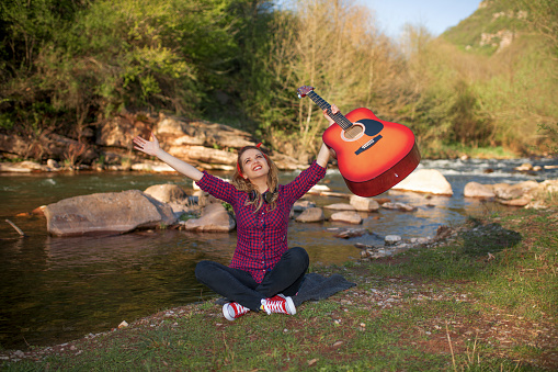 Happy young woman with acoustic guitar enjoying by river