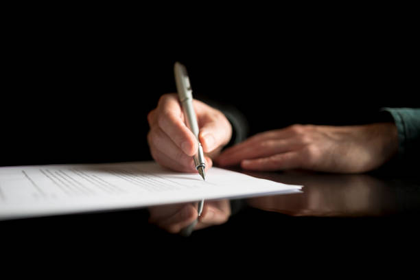 Low view of businessman hand signing legal or insurance document Low view of businessman hand signing legal or insurance document or business contract on black desk with reflection. will legal document stock pictures, royalty-free photos & images