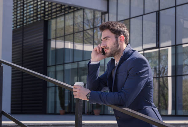 istock one young man, suit tie, talking over phone, outdoors day, modern building 668870662