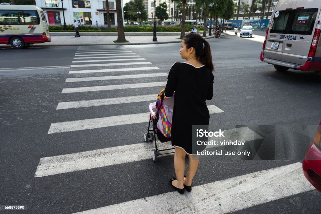 Hanoi, Vietnam - Oct 19, 2016: Mother with a baby stroller crossing the street in Minh Khai. Vehicles running on street Hanoi, Vietnam - Oct 19, 2016: Mother with a baby stroller crossing the street in Minh Khai. Vehicles running on street. Child Stock Photo