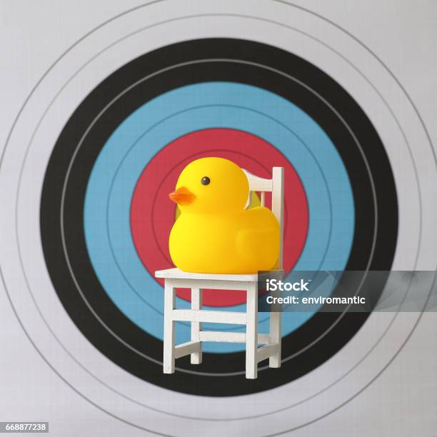 Sitting Yellow Rubber Duck Sitting On A Chair In Front Of The Bullseye Of A Sports Target Stock Photo - Download Image Now