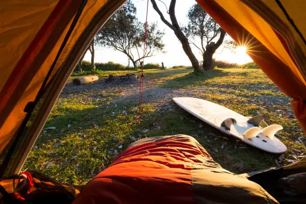 A hikers point of view from a tent, overlooking a bright morning and a surfboard.