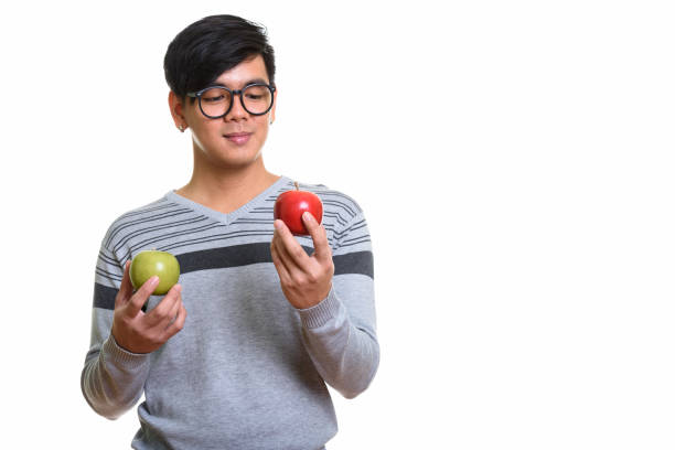 istock Studio shot of handsome Asian man looking at red apple and while holding green apple 668888206