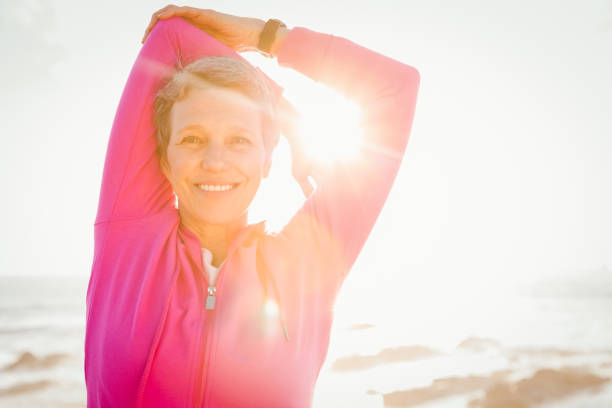 uśmiechnięta sportowa kobieta wyciągająca ramiona na promenadzie - exercising stretching women outdoors zdjęcia i obrazy z banku zdjęć