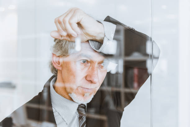 problem fundersam senior affärschef tittar genom fönstret - stressad äldre man bildbanksfoton och bilder