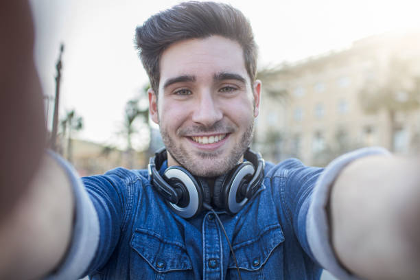 Portrait of handsome man with headphones smiling outdoors. Young male is wearing casuals. He is traveling in city.