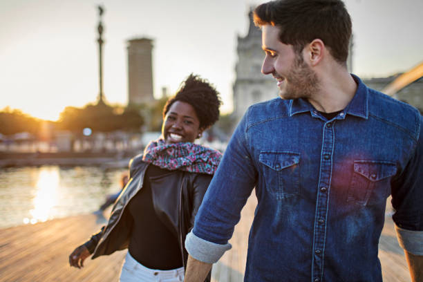 Happy man walking with woman on boardwalk in city Happy man walking with woman on boardwalk. Multi-ethnic couple are wearing casuals. They are hanging out in city. african american architecture stock pictures, royalty-free photos & images