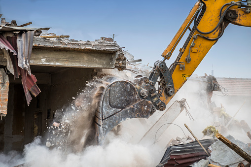 Close of excavator arm demolishing barracks for new construction project. Made with shallow depth of field.