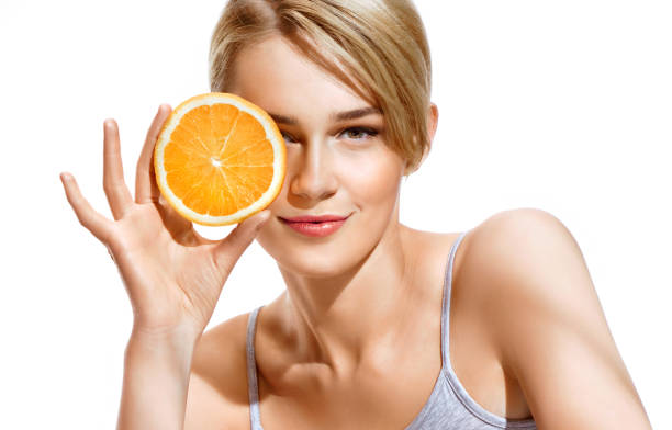 Lovely girl holding a slice of orange in front of her face and smiling stock photo