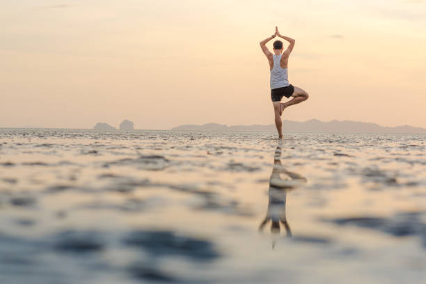 istock Young asian man doing yoga exercise at sunset beach 668965736