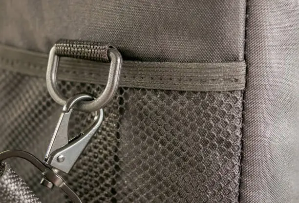 Macro detail of a snap-hook (snap-link) fastened to the black bag with silver loop as a symbol of safety link between two objects.