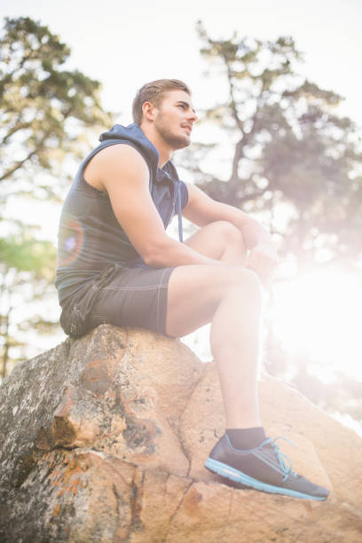 istock Young happy jogger sitting on rock and looking away 669012274