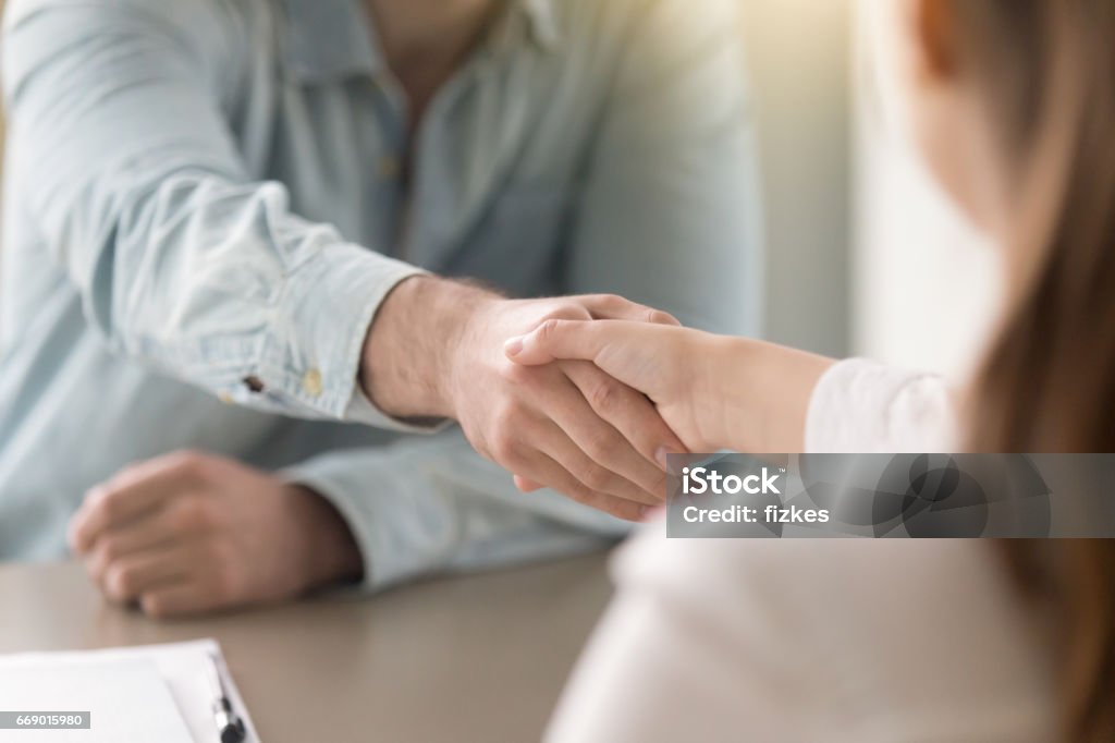 Business agreement handshake of man and woman at the office Businessman shaking female hand above the table. Business agreement and partnership concept. Partners closing a deal, view over the shoulder. Formal greeting gesture, effective negotiations Handshake Stock Photo