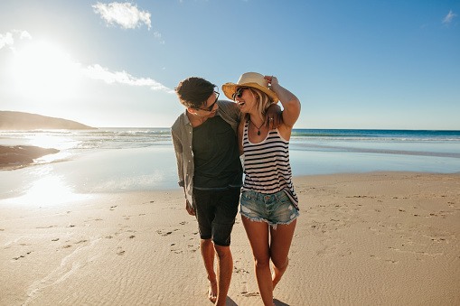 Loving young couple enjoying a day on beach. Beautiful couple walking on the seashore on a summer day.