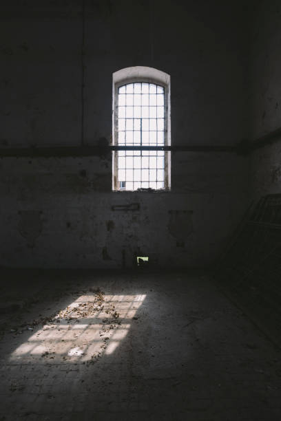 istock Tall window with bars in dark, old abandoned factory hall 669057848