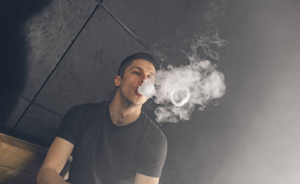 istock Vaping man holding a mod. A cloud of vapor. Black background. 669067314