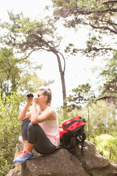 istock Blonde hiker sitting on rock and  looking through binoculars 669068706