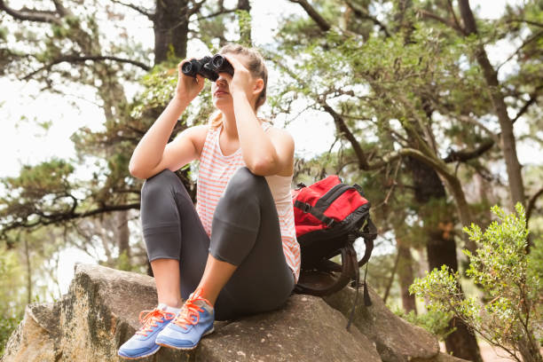 istock Blonde hiker sitting on rock and  looking through binoculars 669068722