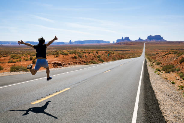 un uomo corre e salta lungo una sezione della highway 163 a monument valley, utah, usa. - corsa di superstrada foto e immagini stock