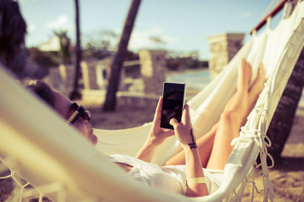 donna che usa il telefono mentre si rilassa su un'amaca - hammock beach vacations tropical climate foto e immagini stock
