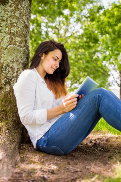 istock Beautiful brunette using tablet pc in the park 669124760
