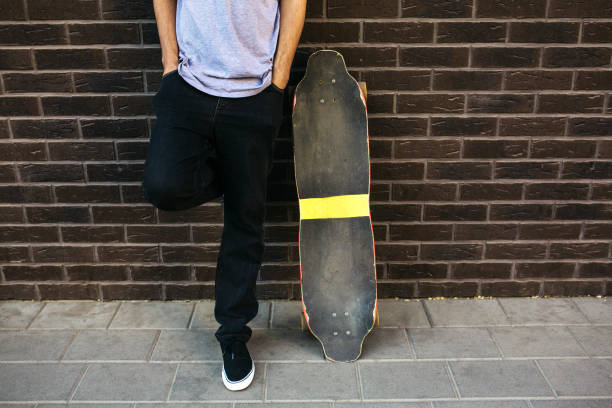 Young adult male walking next to wall with longboard/skateboard