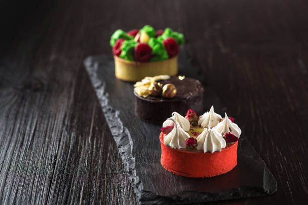 istock Side view on mini party tartlets with fresh fruit, chocolate, nuts and cream on black slate background 669135238