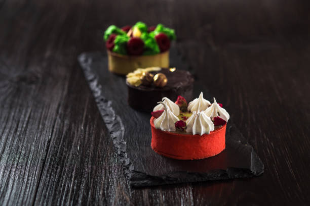 istock Side view on mini party tartlets with fresh fruit, chocolate, nuts and cream on black slate background 669135292