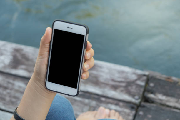 istock Woman with a phone in her hands sitting on pier using smartphone 669161060