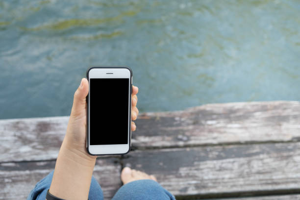 istock Woman with a phone in her hands sitting on pier using smartphone 669161098