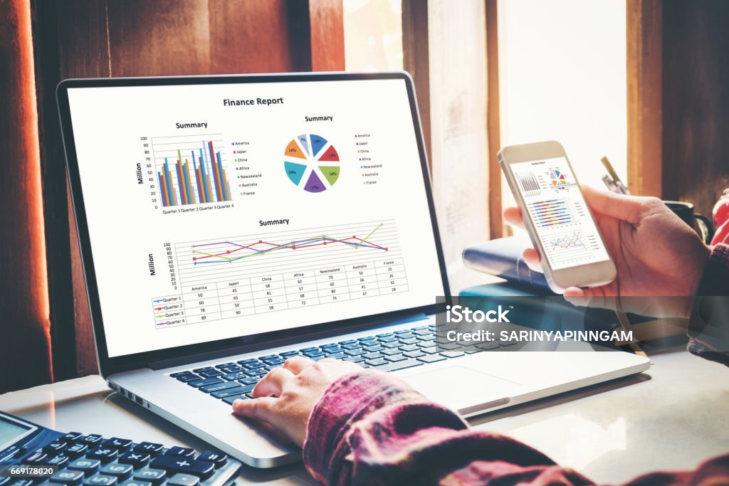 business documents on office  with smart phone and laptop computer and graph financial with social network diagram and three colleagues discussing data in the background Spreadsheet Stock Photo