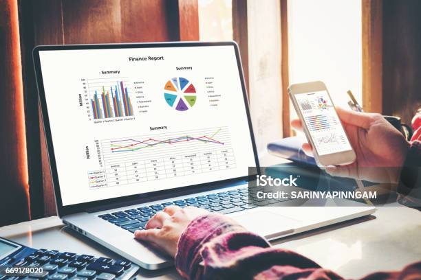 Business Documents On Office With Smart Phone And Laptop Computer And Graph Financial With Social Network Diagram And Three Colleagues Discussing Data In The Background Stock Photo - Download Image Now