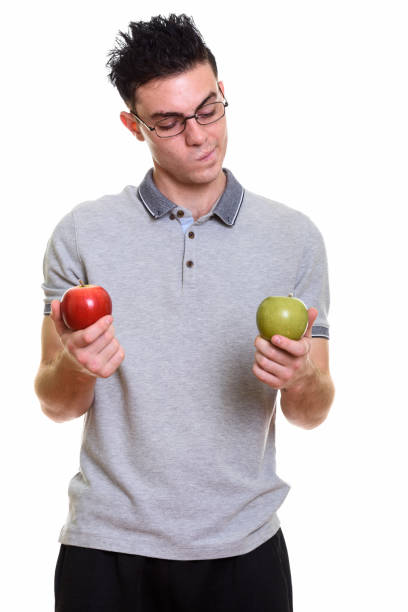 istock Studio shot of young man holding red apple while looking at green apple 669187836