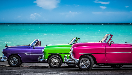 Three colorfully convertible classic cars parked before the Caribbean Sea on the Malecon in Havana Cuba
