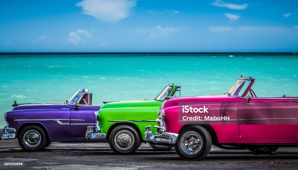 Three colorfully convertible classic cars parked before the Caribbean Sea on the Malecon in Havana Cuba HDR - Three american colorfully convertible vintage cars parked before the caribbean sea on the Malecon in Havana Cuba  - Serie Cuba Reportage Cuba Stock Photo