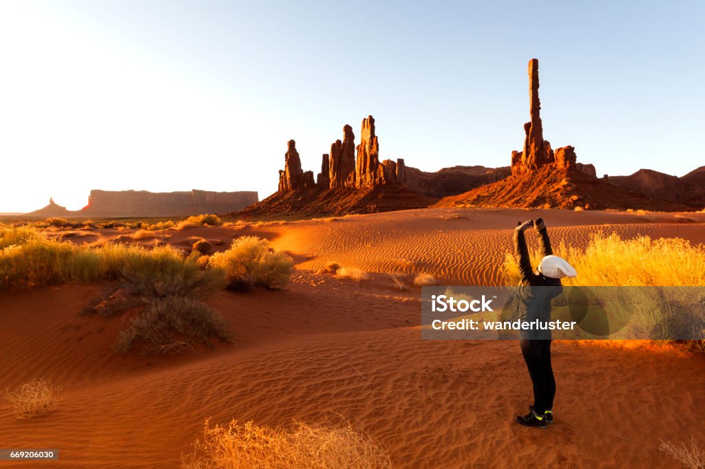Stretching at the Totem Pole at sunrise, Monument Valley, Arizona, USA Teenage girl wearing a winter hat, mittens and coat stretches outdoors on rippled sand at the Totem Pole rock formations at sunrise, Monument Valley, Arizona, USA Landscape - Scenery Stock Photo