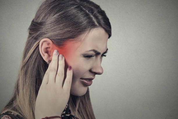 Closeup side profile sick young woman having ear pain touching her painful head temple Tinnitus. Closeup side profile sick young woman having ear pain touching her painful head temple colored in red isolated on gray background neuralgia stock pictures, royalty-free photos & images