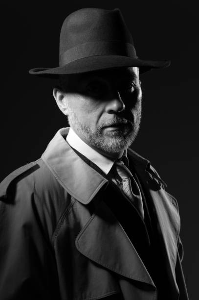 Confident man wearing a fedora hat and a trench coat, he is looking at camera, 1950s noir movie style